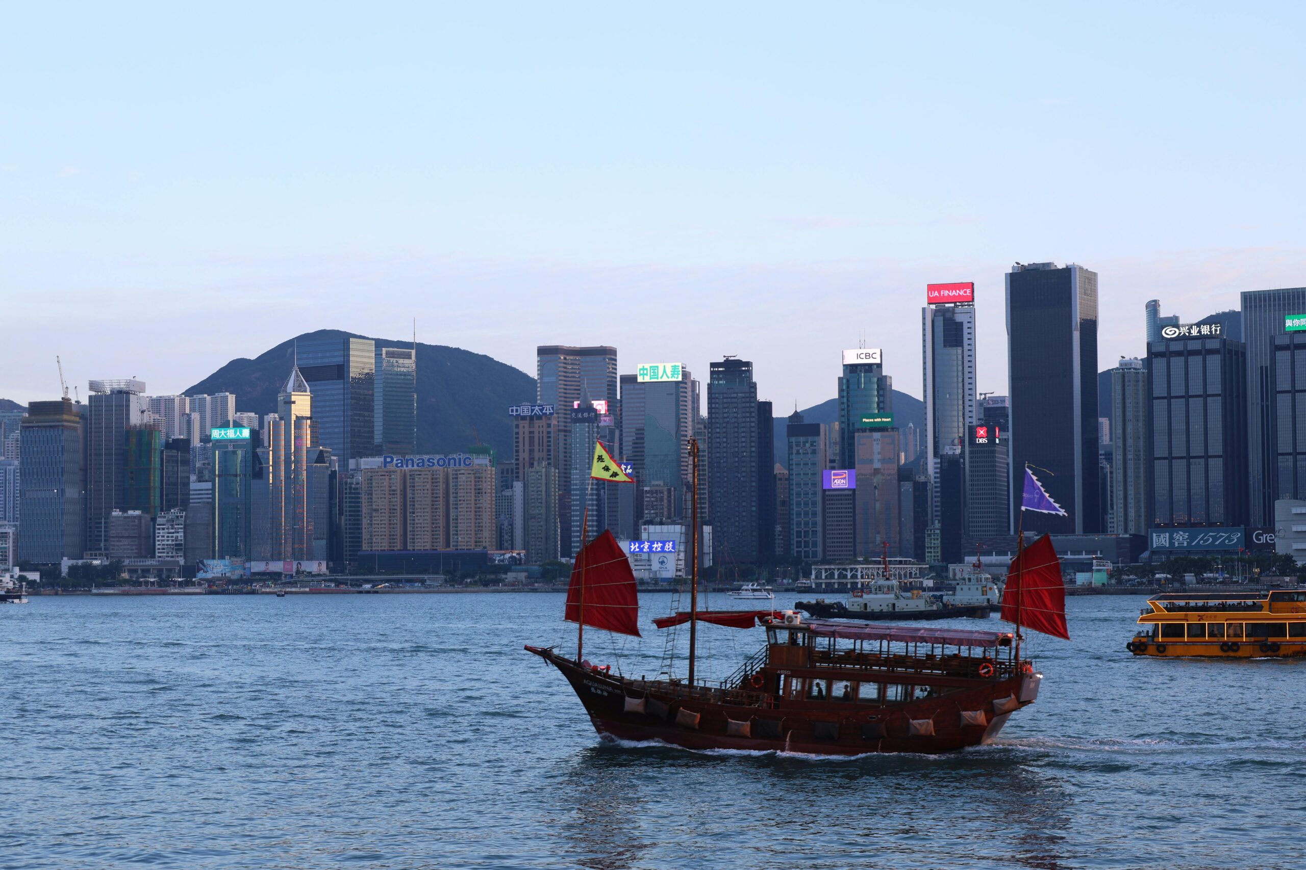 A picturesque view of a traditional junk boat sailing past Hong Kong's modern skyline at dusk.